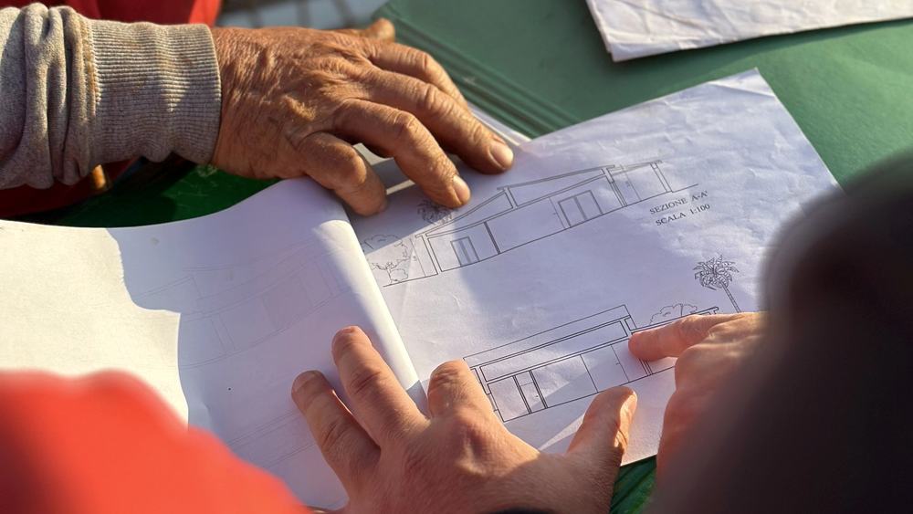 Hands reviewing a technical construction drawing spread across a work table.