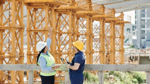 Two construction workers in high-visibility vests on a timber-framed building under construction.