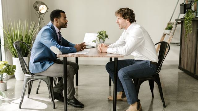 A business owner and an advisor talking across a table in a modern office.