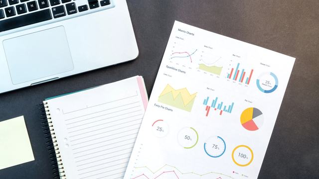 A printed financial report with charts and summary figures lying beside a laptop and notebook.